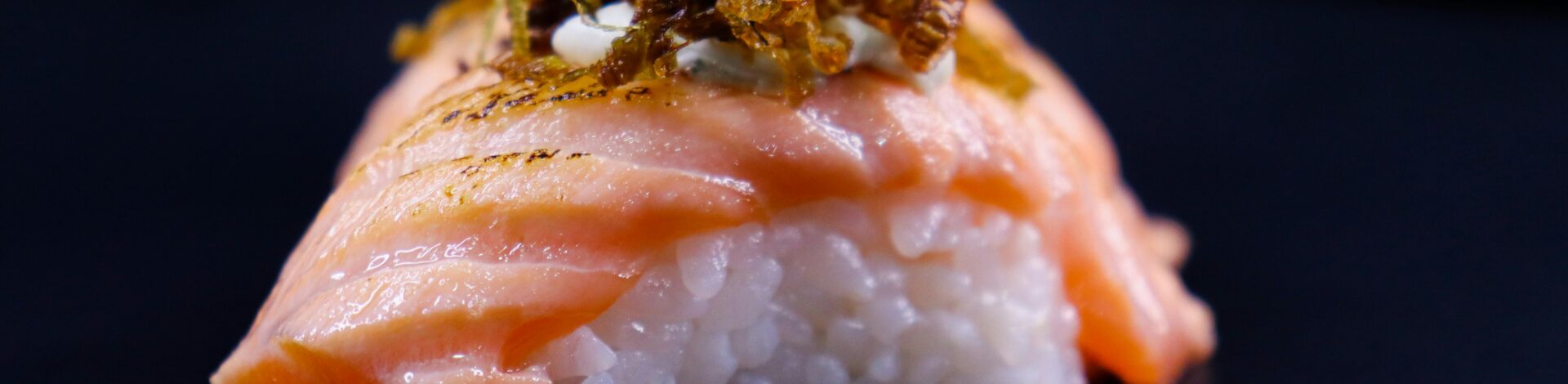 Close-up of a gourmet salmon nigiri sushi with rice and fried onions.