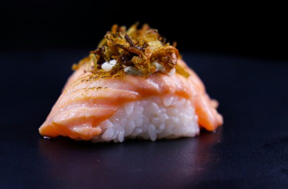 Close-up of a gourmet salmon nigiri sushi with rice and fried onions.