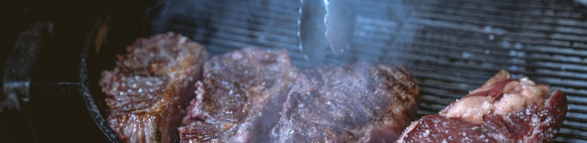 Close-up of juicy steaks sizzling on a smoky barbecue grill, ideal for a food or lifestyle theme.