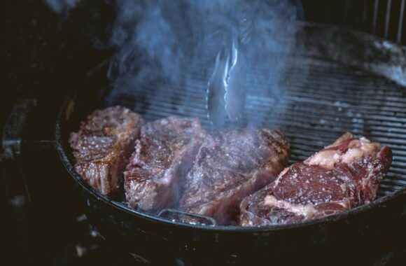 Close-up of juicy steaks sizzling on a smoky barbecue grill, ideal for a food or lifestyle theme.